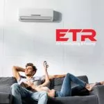 a couple is lying on a couch. a white aircondition and ETR logo are on a white wall above them.