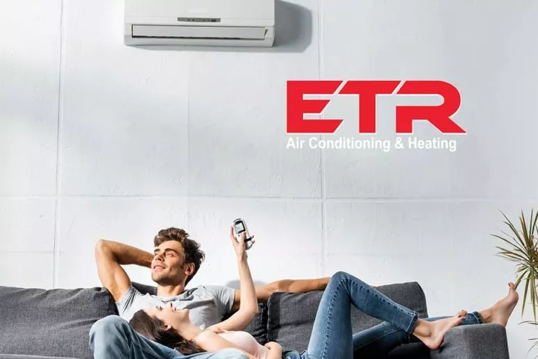 a couple is lying on a couch. a white aircondition and ETR logo are on a white wall above them.